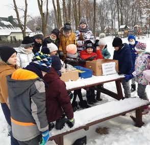Dzieci na dworze, stoją wokół stołu, na stole przygotowana żywność dla zwierząt